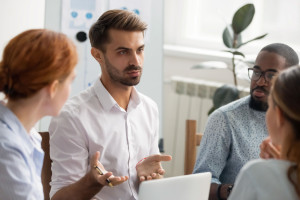 Serious businessman talking with group of business partners at meeting