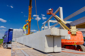 Worker is attaching crane hooks to concrete joist in truck trail