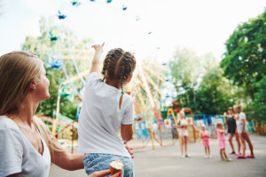 Eating ice cream. Cheerful little girl her mother have a good time in the park together near attractions