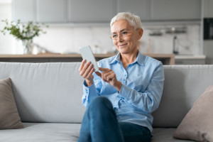 Senior Lady Wearing Eyeglasses Using Internet On Smartphone Texting Indoor