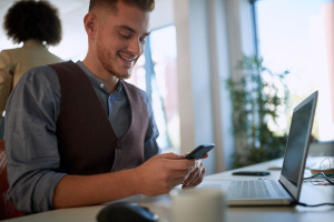 young employee watching his cell phone, smiling, on his workplac