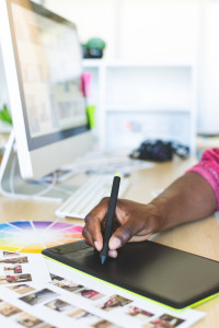 Close-up of young African-American graphic designer working on graphic tablet at desk in office