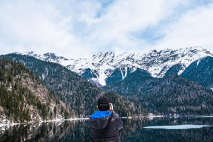 A man photographs a mountain landscape. Lake Ritsa in the spring season. Located in Abkhazia, in the mountains of the Caucasus.