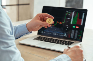 Cropped shot of trader investor holding bitcoin, using laptop, investing in cryptocurrency