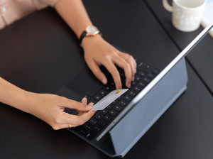 Female online paying, hand typing on tablet keyboard and holding credit card